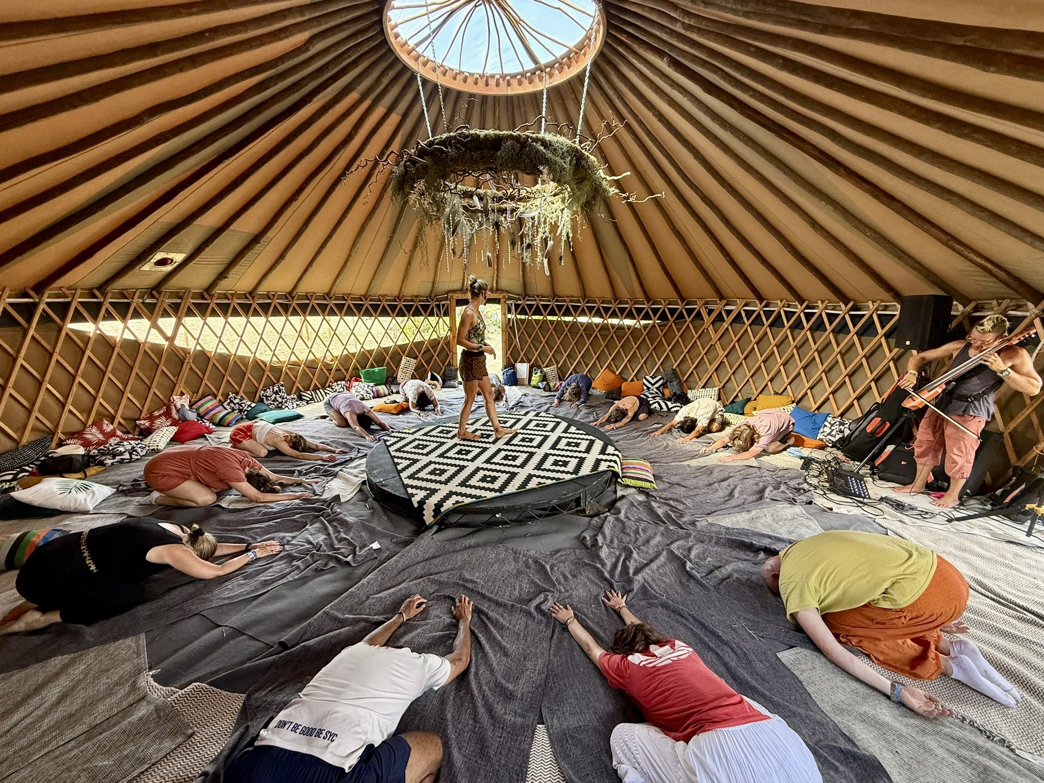 A room of practitioners resting forward on their mats while a cellist plays